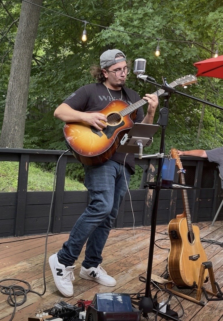 Jacob Smith performing acoustic guitar on a backyard deck under string lights